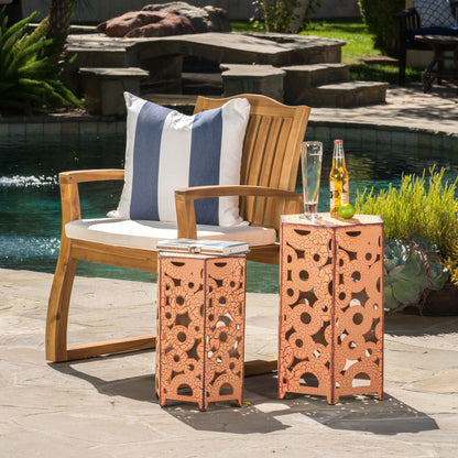 A wooden patio chair with a white and blue striped pillow sits by a pool. Two Selva - Accent Tables hold a notebook, pen, champagne glass, and a bottle of beer with a lime wedge.