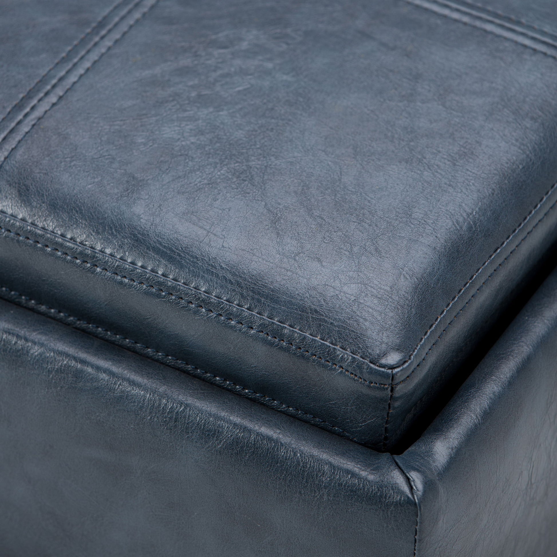 Close-up of the Rockwood - Upholstered Cube Storage Ottoman With Tray in dark blue leather, highlighting its detailed stitching and soft, textured surface.
