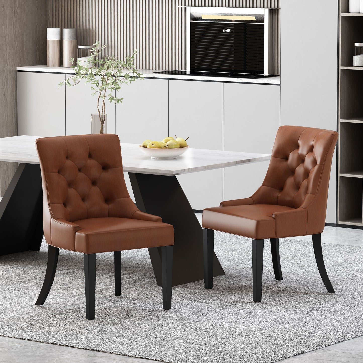 Two Cheney Contemporary Dining Chairs with tufted brown upholstery and black legs are placed by a modern white dining table, complemented by a light gray rug, decorative plant, minimalist kitchen backdrop, and a bowl of lemons.