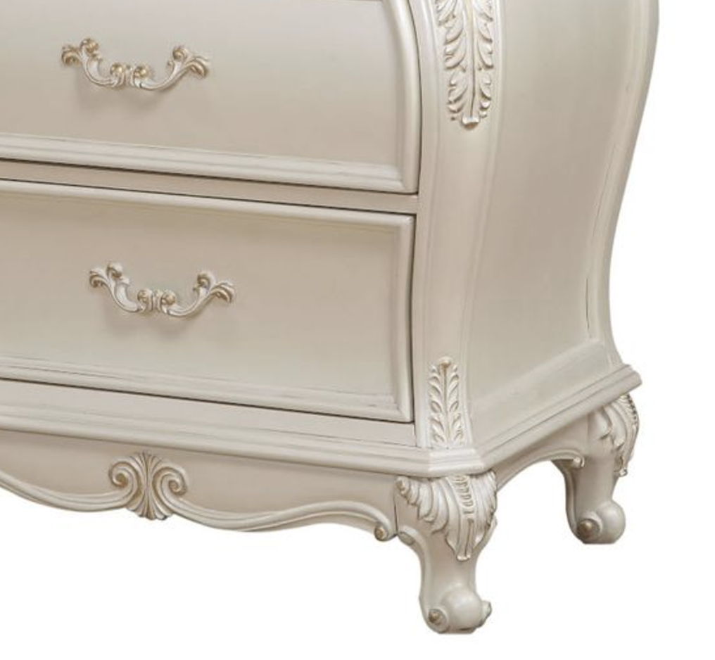 The Chantelle nightstand showcases a vintage style with intricate floral carvings and decorative handles. It’s painted in an elegant white finish and features curved legs and a classic, sophisticated design, topped with granite for added elegance.