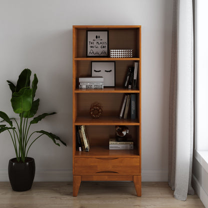 The Harper - Handcrafted Bookcase With Storage, styled with books, decor, and framed prints, stands on a light wood floor next to a leafy potted plant by a window with sheer white curtains.