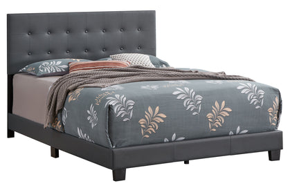 The Caldwell - Bed features a tufted dark gray upholstered headboard, gray floral-patterned bedding, a brown knit throw, and assorted pillows, all set against a white background.