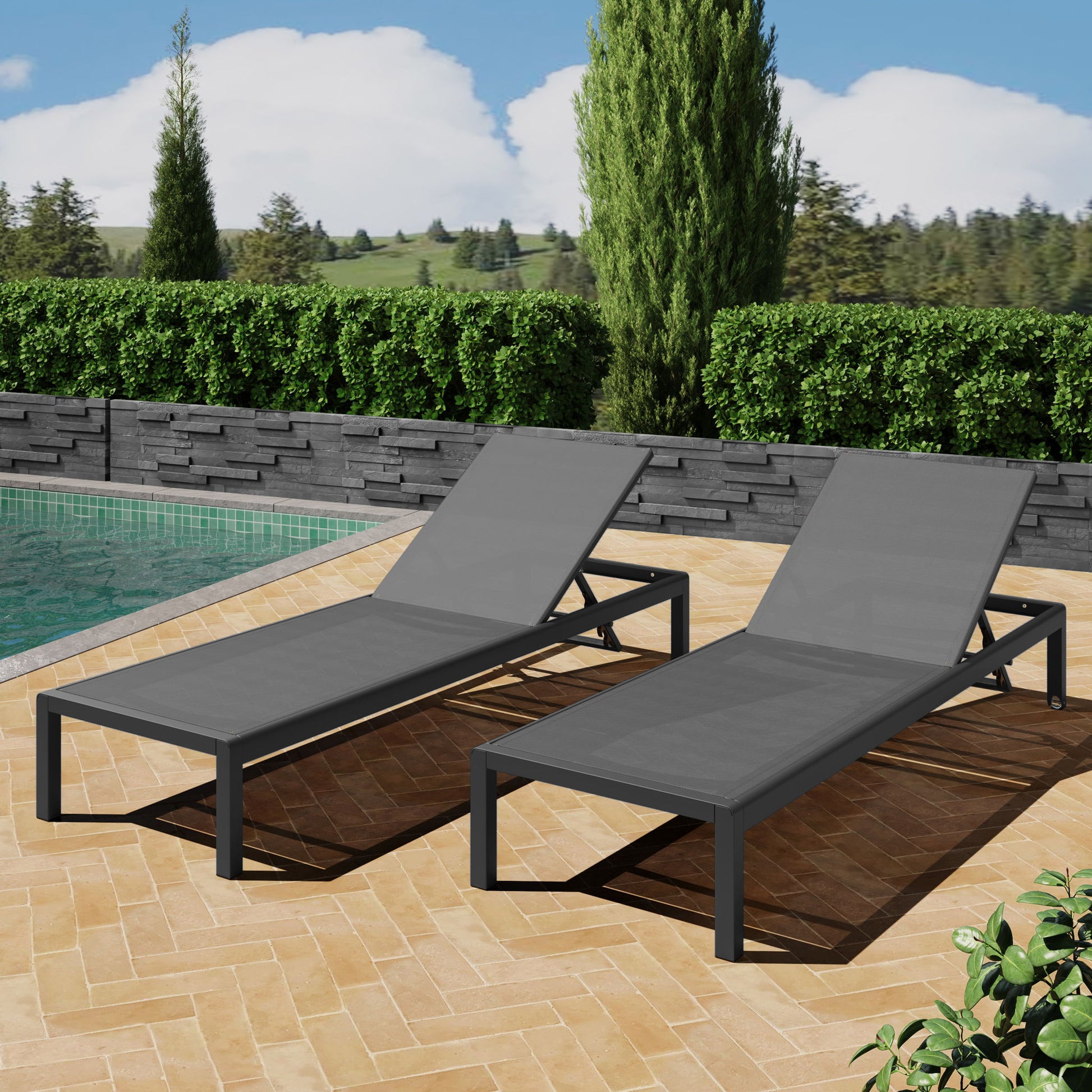 Two Outdoor Patio Chaise Lounges with 5 Reclining Positions in modern gray sit on a tan herringbone patio by the pool, surrounded by green hedges, trees, and grassy fields under a partly cloudy sky.