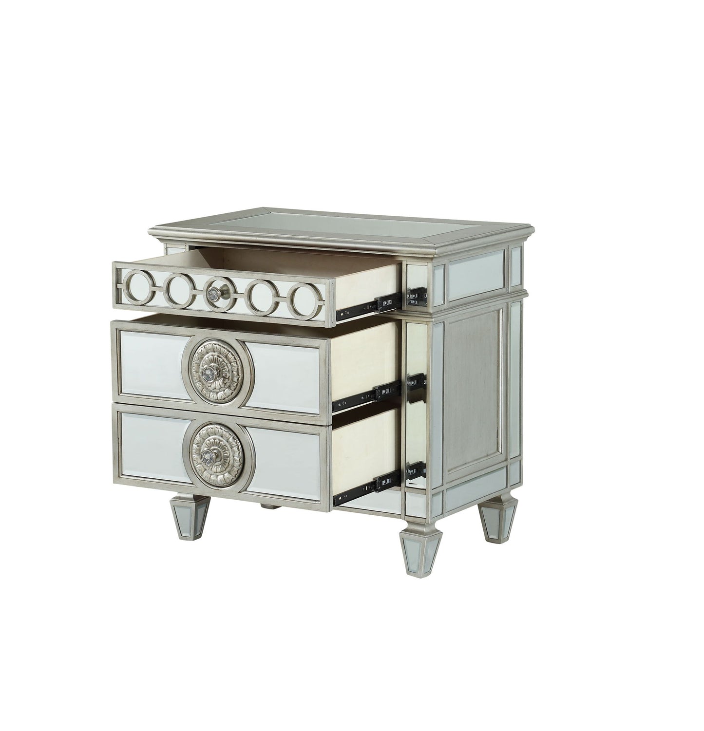 The Varian Mirrored Nightstand in silver features three drawers with ornate circular handles, reflective panels on the surface and sides, and short, angled legs; two drawers are shown open.