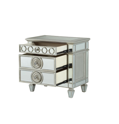 The Varian Mirrored Nightstand in silver features three drawers with ornate circular handles, reflective panels on the surface and sides, and short, angled legs; two drawers are shown open.