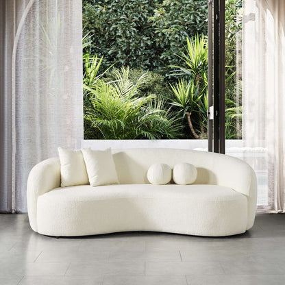 The Drake - Japandi Style Curvy Boucle Sofa in modern white, featuring three cushions, sits on a gray tile floor before large windows with sheer curtains, overlooking lush greenery.