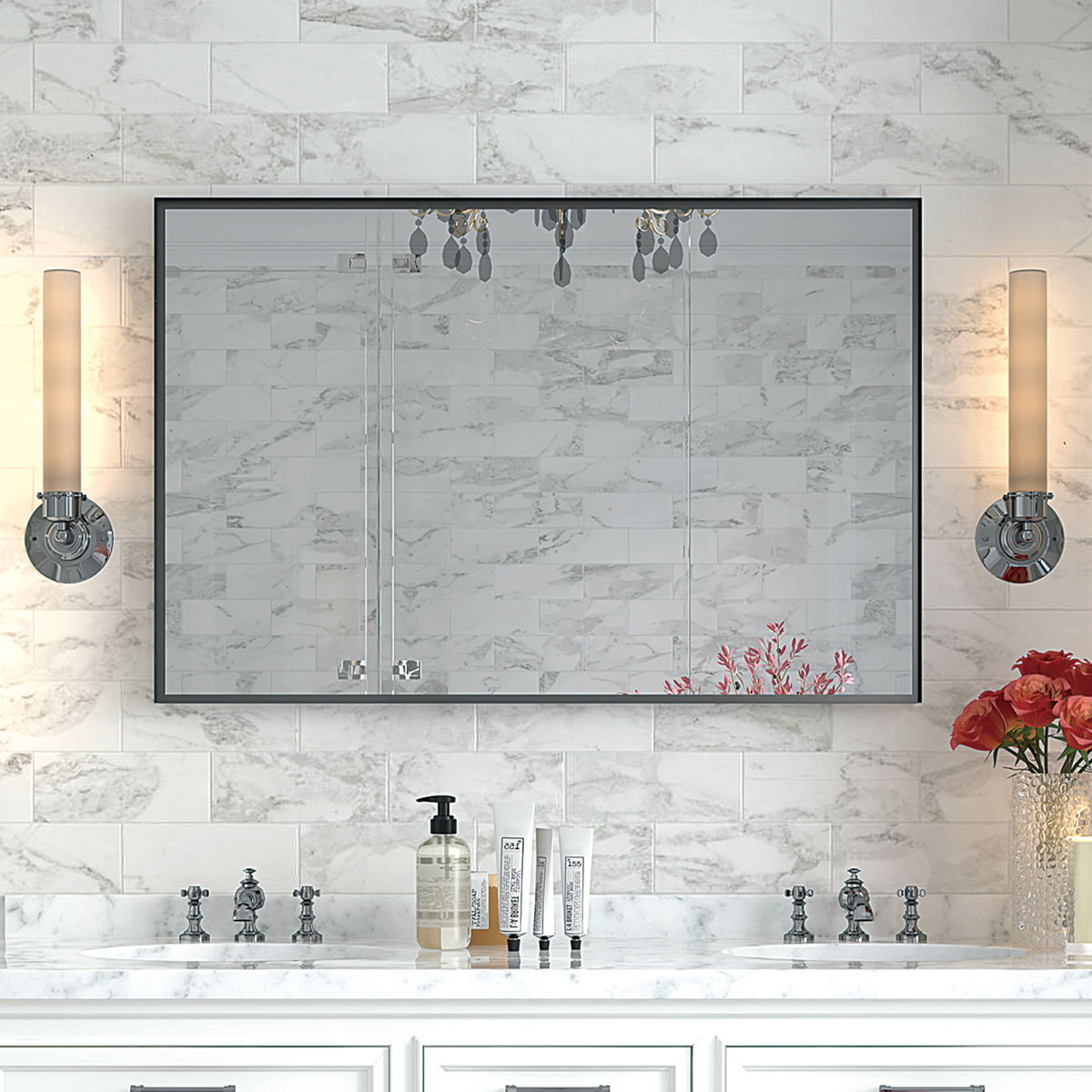 A bathroom vanity features the Rectangular Bathroom Mirror with a square angle metal frame, wall mounted above a white marble countertop with silver faucets, skincare products, red flowers in a vase, and two cylindrical lights. White marble tiles cover the wall.