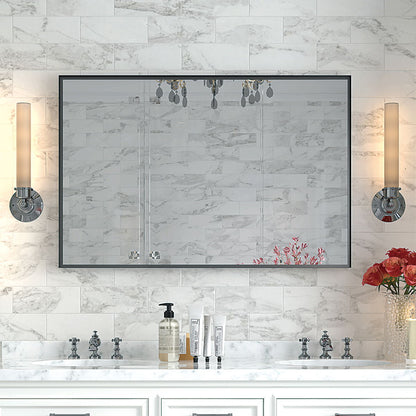 A bathroom vanity features the Rectangular Bathroom Mirror with a square angle metal frame, wall mounted above a white marble countertop with silver faucets, skincare products, red flowers in a vase, and two cylindrical lights. White marble tiles cover the wall.