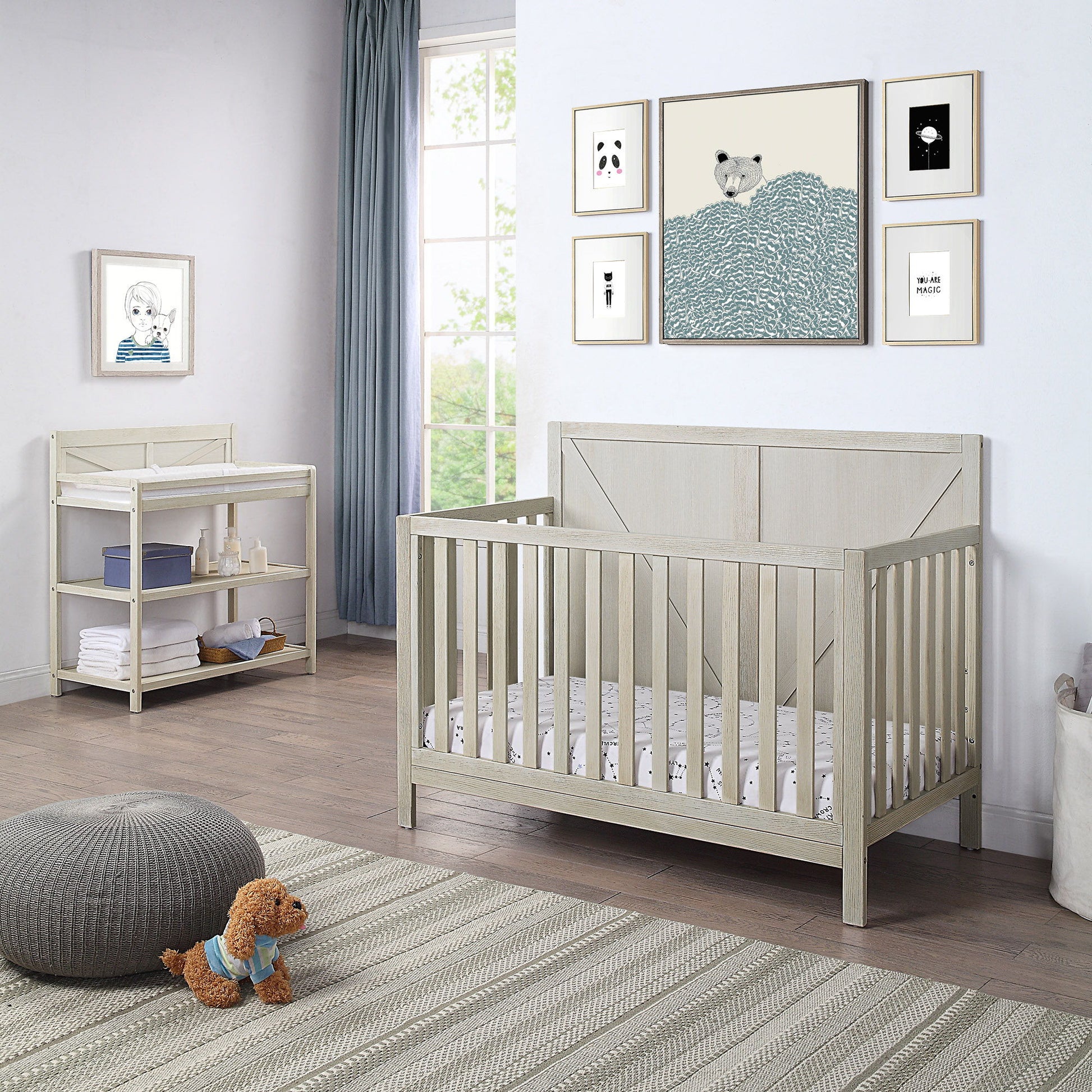 A bright, modern nursery with a light wood crib, the Barnside - Changing Table Vintage, plush rug, small stuffed dog, and framed animal prints. Sunlight streams through a large window with light blue curtains.