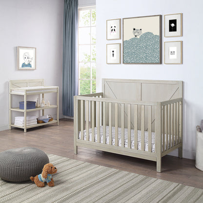 A bright, modern nursery with a light wood crib, the Barnside - Changing Table Vintage, plush rug, small stuffed dog, and framed animal prints. Sunlight streams through a large window with light blue curtains.