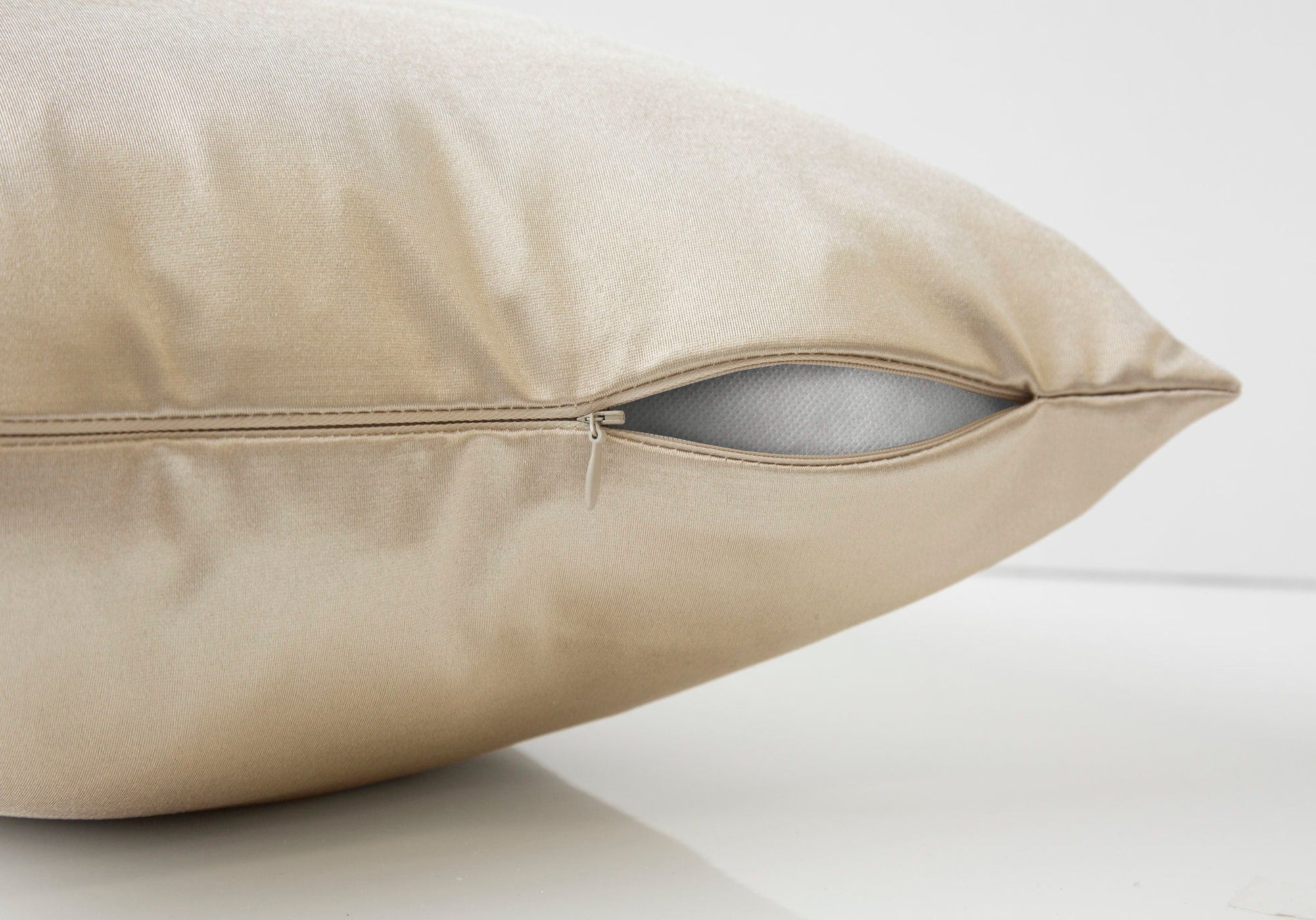 A close-up of a beige decorative throw pillow (square, insert included) with a partially open zipper revealing its white hypoallergenic inner lining. The background is plain and light-colored, highlighting its modern design.