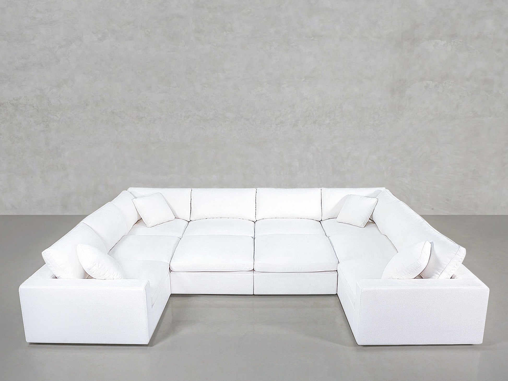 A spacious, modern white 10-Seat Modular Closed Pit sectional with four matching white throw pillows, set against a plain light gray wall and smooth gray floor.