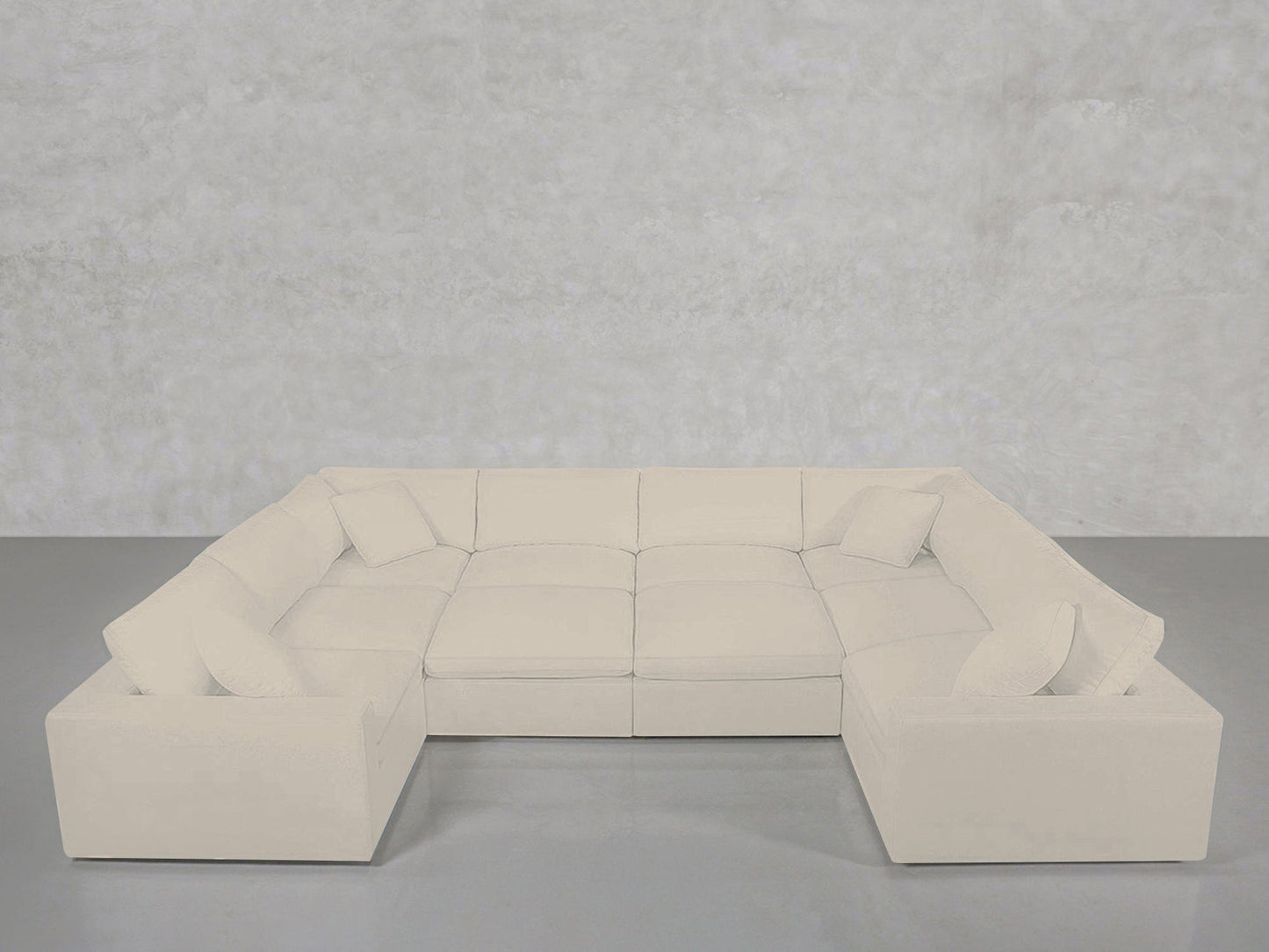 A spacious, light cream 10-Seat Modular Closed Pit sectional with plush cushions and matching throw pillows, arranged against a plain light grey wall and floor.