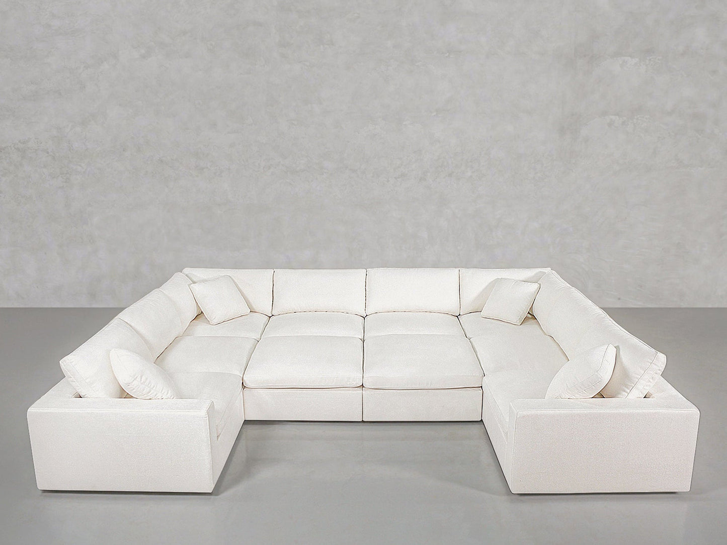 Spacious 10-Seat Modular Closed Pit sectional sofa in modern white, featuring six seat cushions and four matching throw pillows, placed before a plain light gray wall and smooth gray floor.
