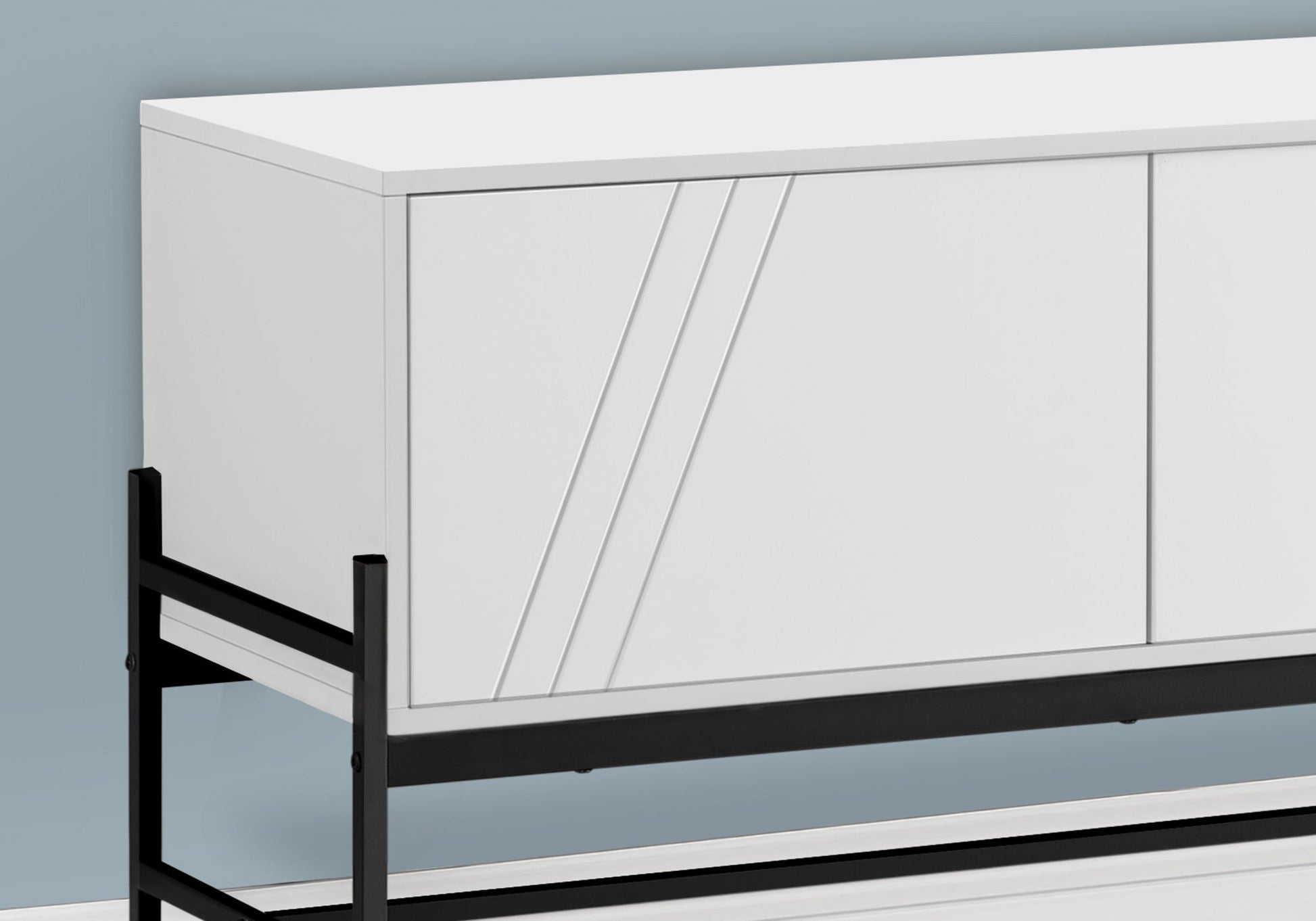 A contemporary white TV stand and storage cabinet with sleek diagonal accents on the doors, featuring a black metal frame, placed against a light blue wall.