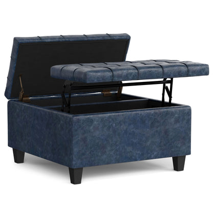 The Harrison Upholstered Coffee Table Storage Ottoman features a blue square design with black legs, a lift-top lid revealing interior storage, and tufted cushioning shown partially raised.