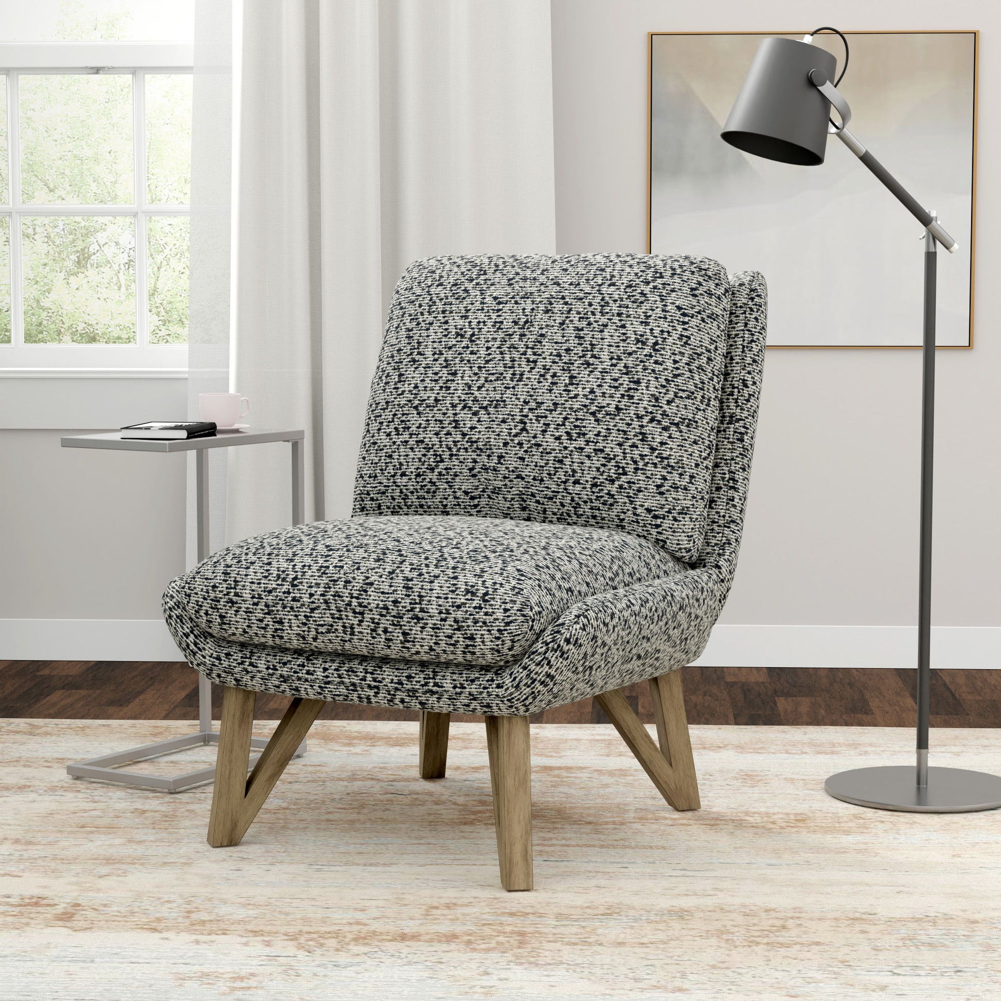 The Emerse Armless Accent Chair in blue sits on a light rug next to a small metal side table and a black floor lamp in a bright room with a window and white curtains.
