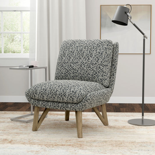 The Emerse Armless Accent Chair in blue sits on a light rug next to a small metal side table and a black floor lamp in a bright room with a window and white curtains.