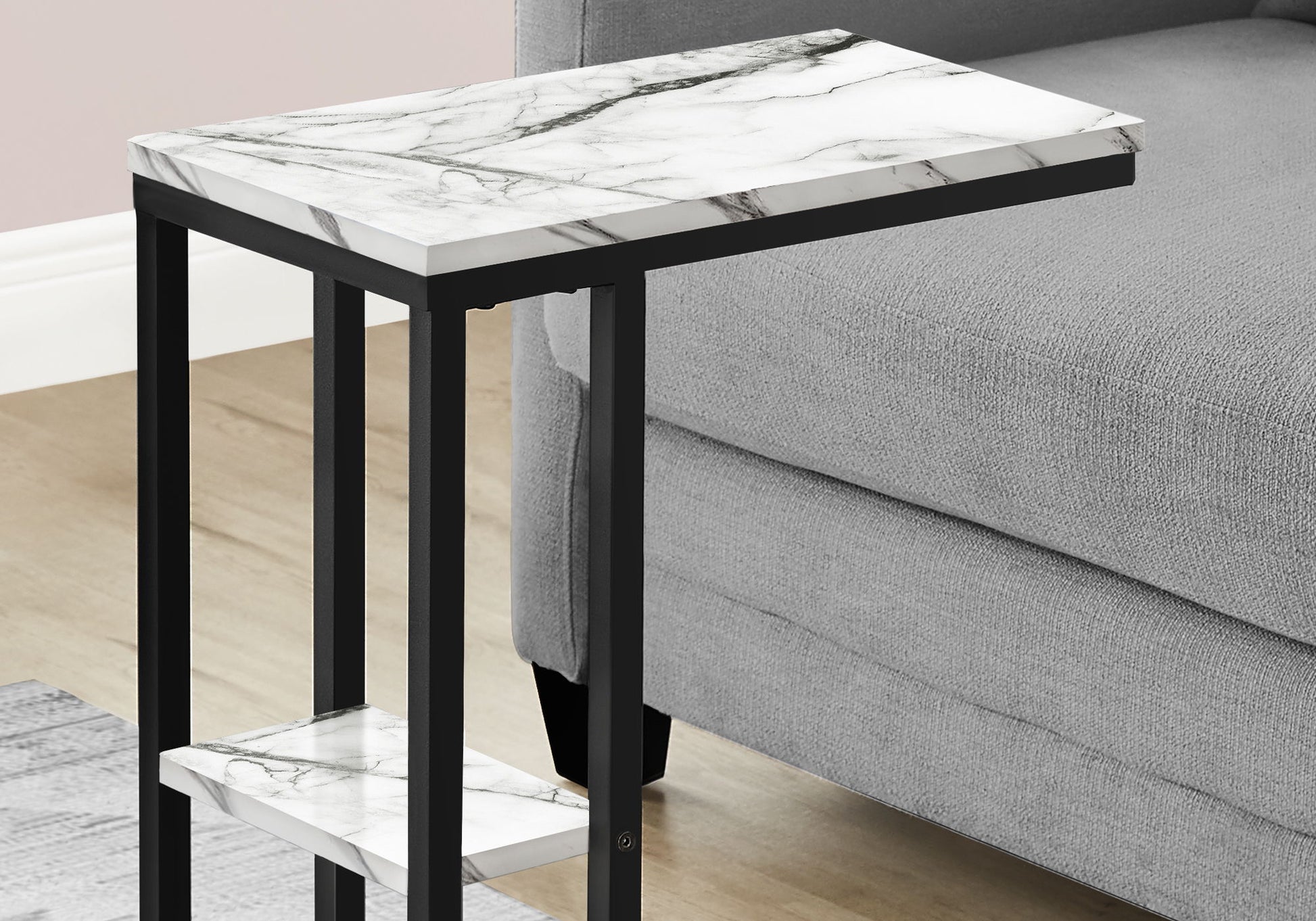 The Accent Table C - Shaped, Contemporary & Modern features a white marble-patterned top and black metal frame, shown beside a light gray upholstered sofa on a wooden floor.