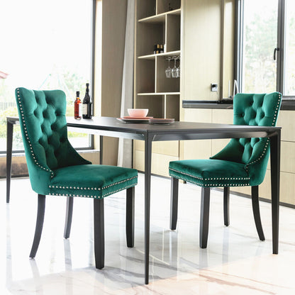 Two Nikki tufted velvet dining chairs with nailhead trim stand at a black rectangular table in a bright, modern kitchen with large windows and marble floors. Wine bottles and glasses decorate the table and shelves.