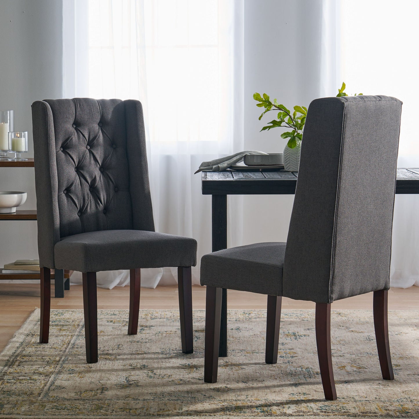 Two Sophisticated Tufted Dining Chairs With High Back Design and wooden legs sit on a patterned rug near a dining table in a bright room with sheer white curtains and abundant natural light.