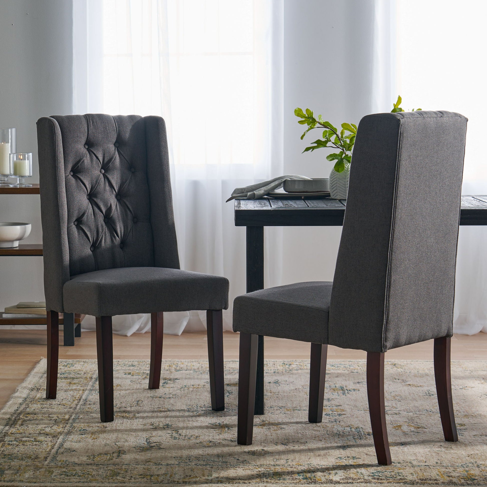 Two Sophisticated Tufted Dining Chairs With High Back Design and wooden legs sit on a patterned rug near a dining table in a bright room with sheer white curtains and abundant natural light.
