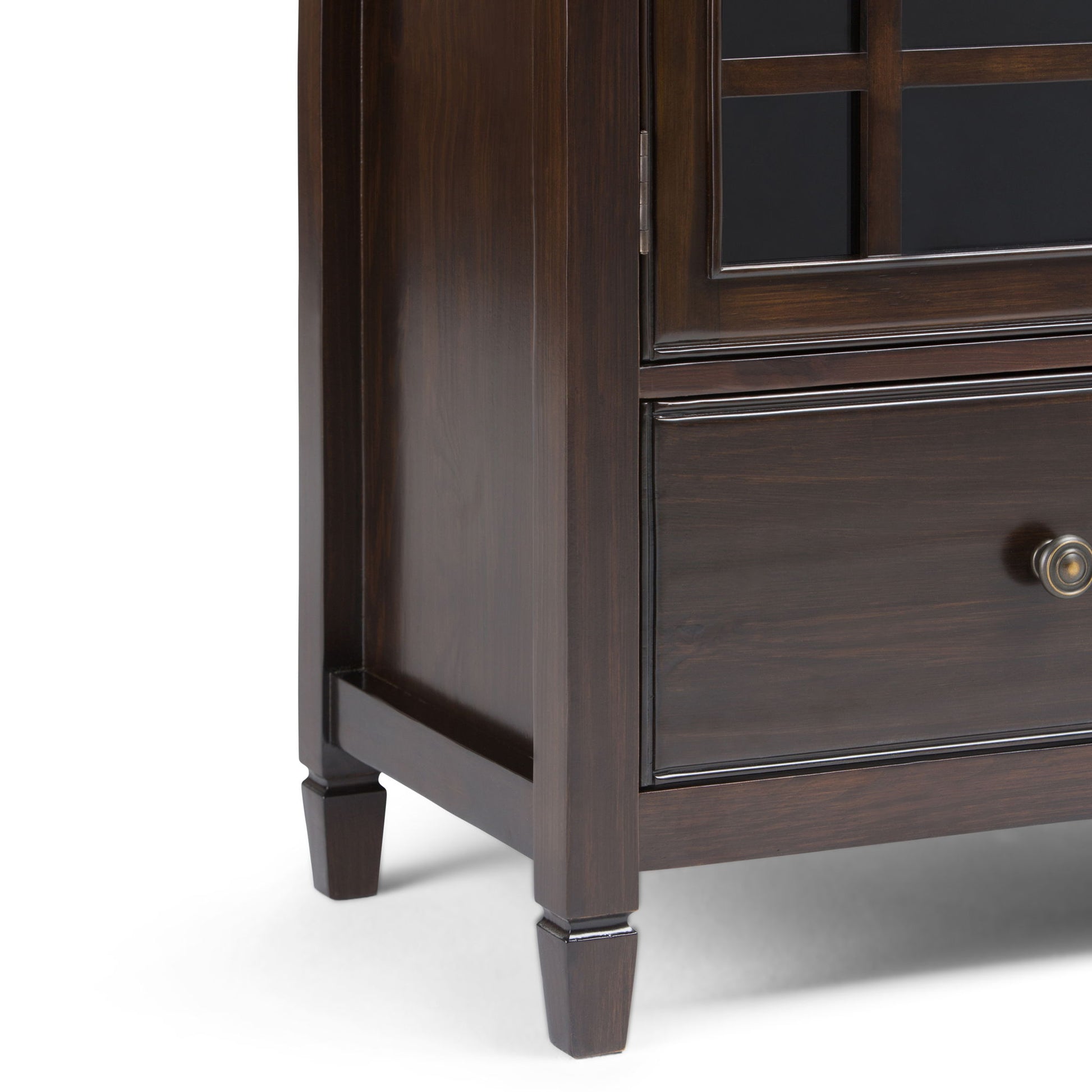 Close-up of the Connaught Tall Storage Cabinet in Dark Chestnut Brown, showing its lower corner with a drawer, glass-paned door, round metal knob, and square tapered legs against a white background.
