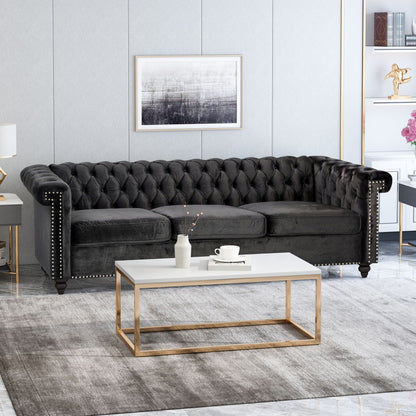 A modern living room featuring a Chesterfield Style 3 Seater Sofa With Deep Button Tufting, a white and gold coffee table, gray rug, abstract wall art above the sofa, and side shelves with decorative items and books.
