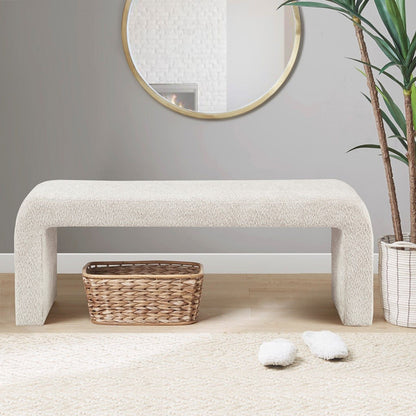 The Modern Contemporary Waterfall Bench - Cream sits on a wooden floor with a woven basket underneath. Above, a round mirror hangs on the gray wall, with a green plant and fluffy slippers nearby.