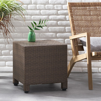 The Puerta - Minimalist Style Accent Table with a small green vase and plant sits beside a wooden chair with a woven back and gray cushion, against a white brick wall and gray floor. A potted plant is on the left.