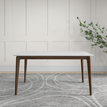 The Levi - Modern Style Rectangular Dining Kitchen Table, featuring a white top and dark wooden legs, stands on a gray patterned rug before a white paneled wall, with a vase holding green leaves on the right.