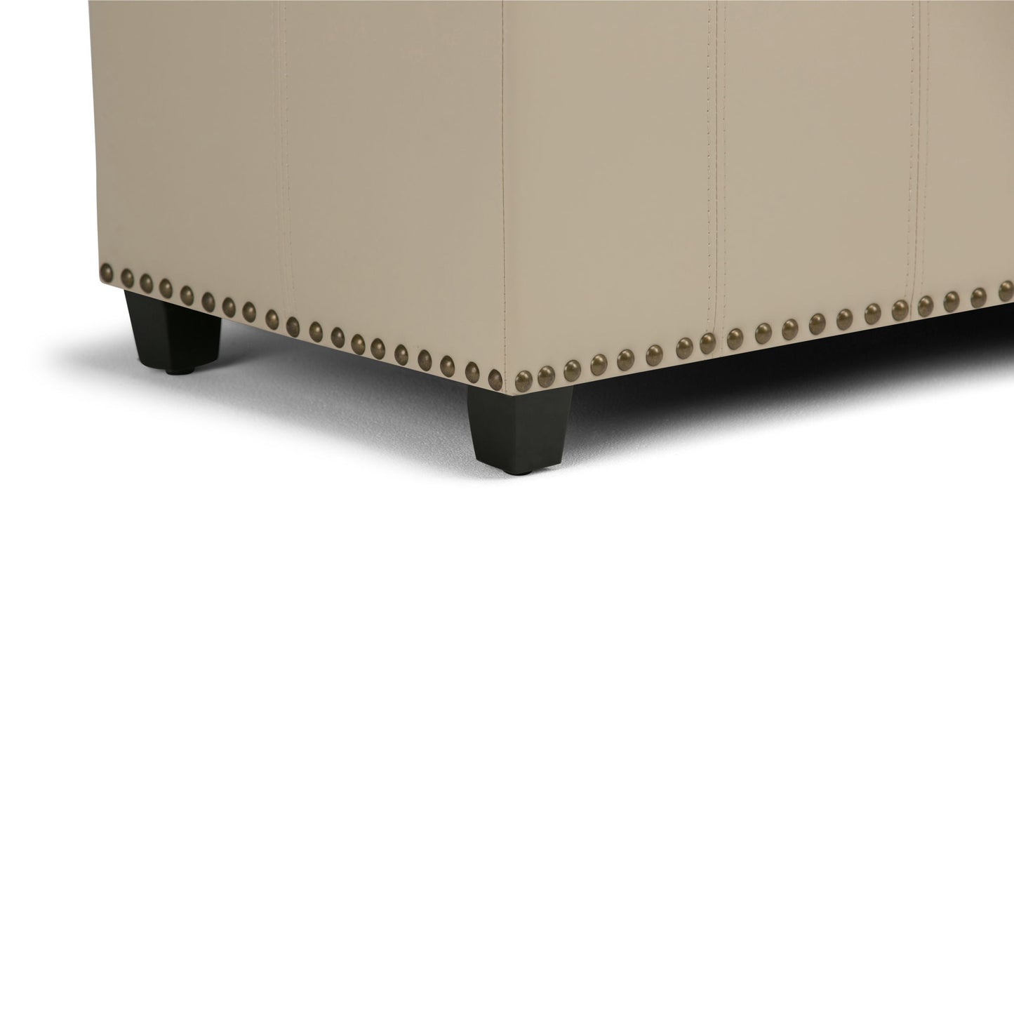 Close-up of the bottom corner of the Amelia - Transitional Storage Ottoman Bench, featuring beige upholstery, decorative nailhead trim, and dark wooden legs on a white background.