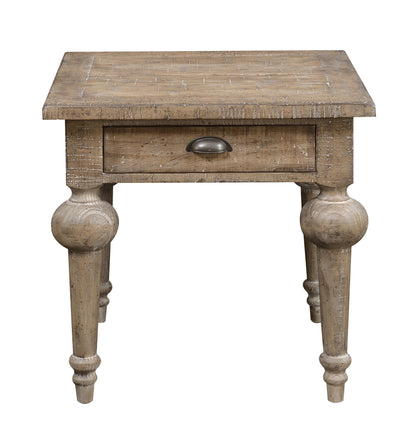 The Ludin - Table is a rustic wooden end table featuring a single drawer with a metal cup pull, four turned legs, and a weathered, distressed finish that highlights its vintage style.