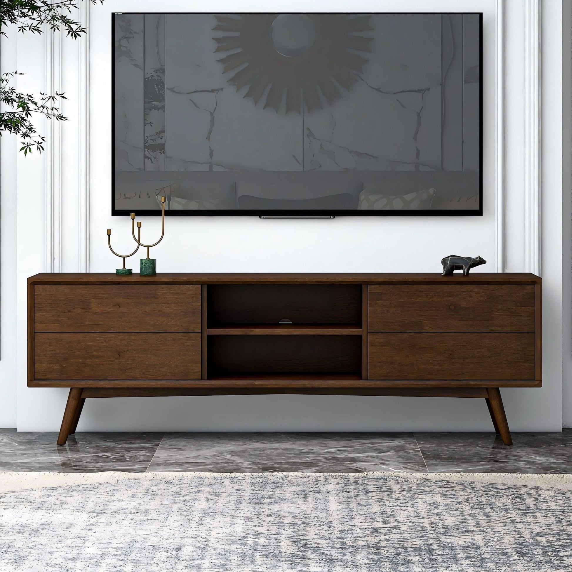 A modern living room with a wall-mounted flat-screen TV above the Caroline - Modern TV Stand Up To 72", decorated with a gold candelabra and a small bear figurine.