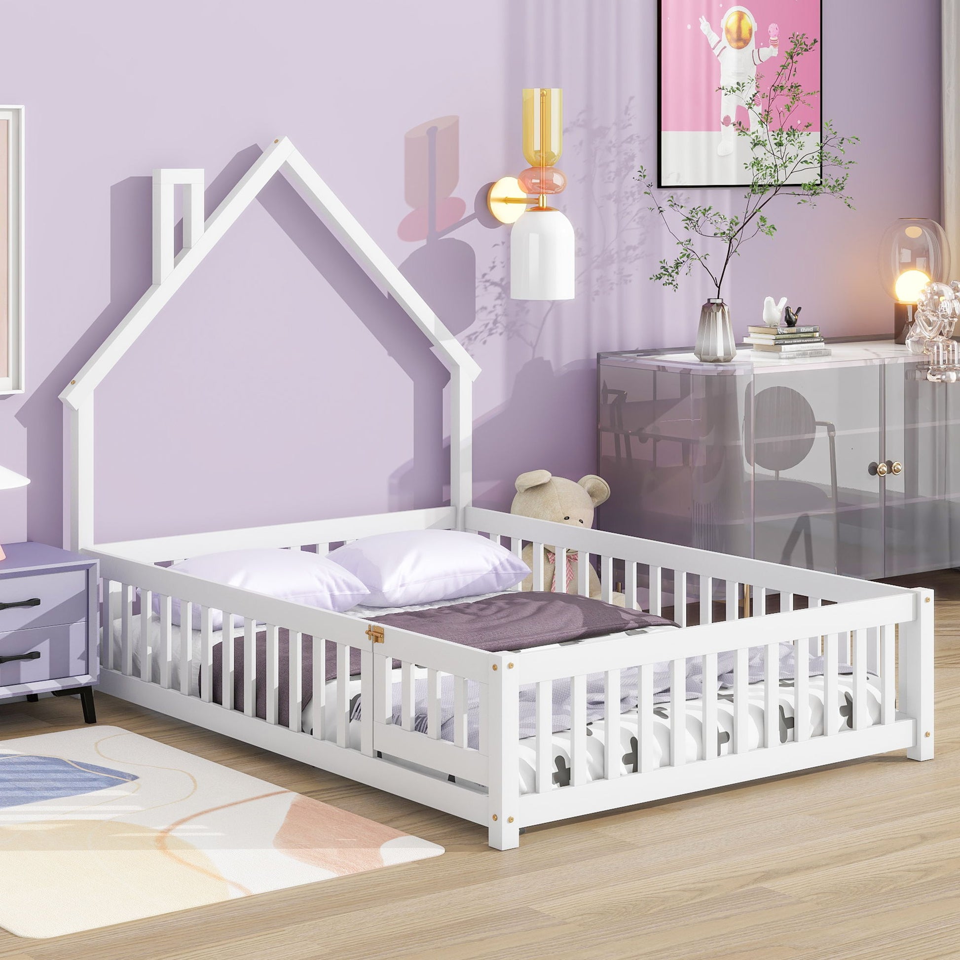 The House-Shaped Headboard Floor Bed With Fence, a white children’s bed with safety rails, is featured in a purple-themed bedroom adorned with pillows, a stuffed bear, wall art, and modern decor.