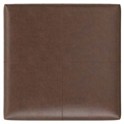 The Gabbie Coffee Table Upholstered Storage Ottoman features a square, brown leather-upholstered cushion with visible cross-pattern seams and a smooth, slightly textured surface.