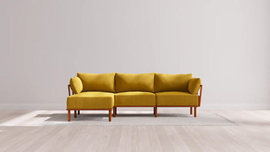 Yellow three-seater sofa with wooden armrests and legs on a light gray rug, set against a neutral wall and light hardwood floor.