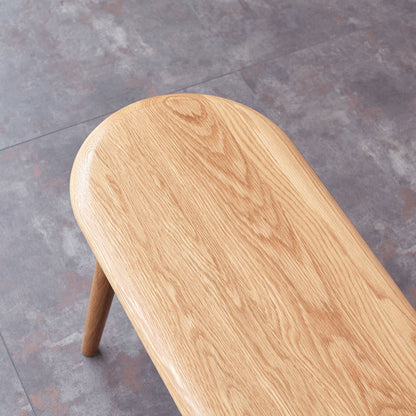 The Dining Bench, Table Bench For Living Room features rounded edges and visible wood grain. Shown partially on a gray and brown tiled floor, only the seat and one leg of the bench are visible.