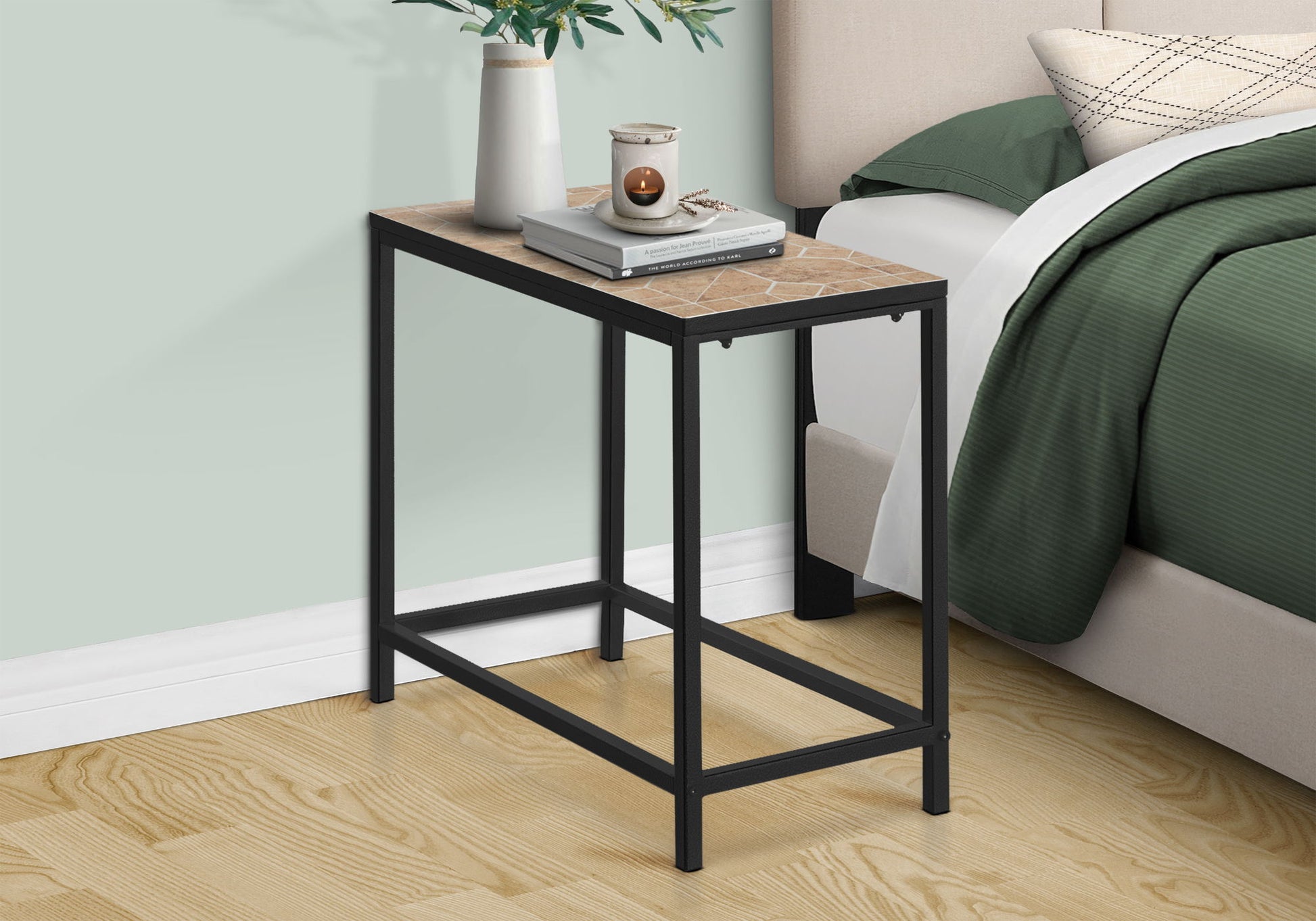 The Perfect Accent Table, Side Transitional with a metal frame and wood-patterned top stands by a bed with green bedding. On the table are a plant, candle, and books. The room has light wood flooring.