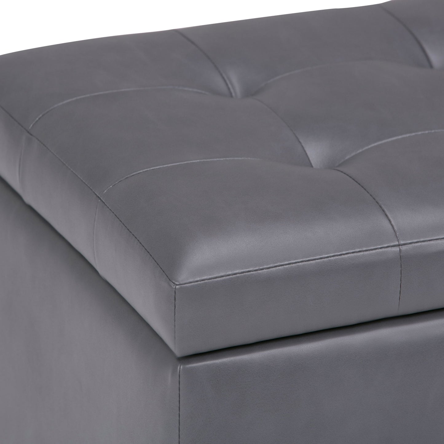 Close-up of the Cosmopolitan Upholstered Storage Ottoman in gray faux leather, featuring a tufted, cushioned top with square stitching.