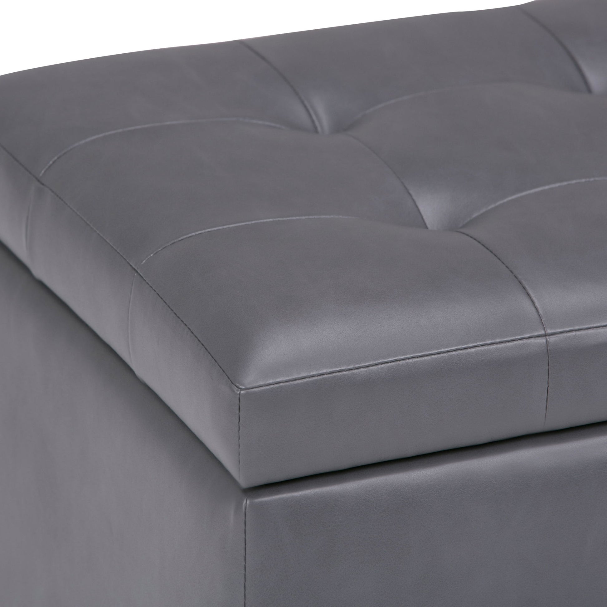 Close-up of the Cosmopolitan Upholstered Storage Ottoman in gray faux leather, featuring a tufted, cushioned top with square stitching.