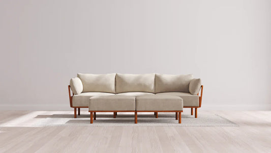 The Indoor Jack 3-Seater Sofa + Bench Ottoman in Balsa features prominently on a textured light gray rug within a minimalist room, complemented by pale wood flooring and plain white walls.