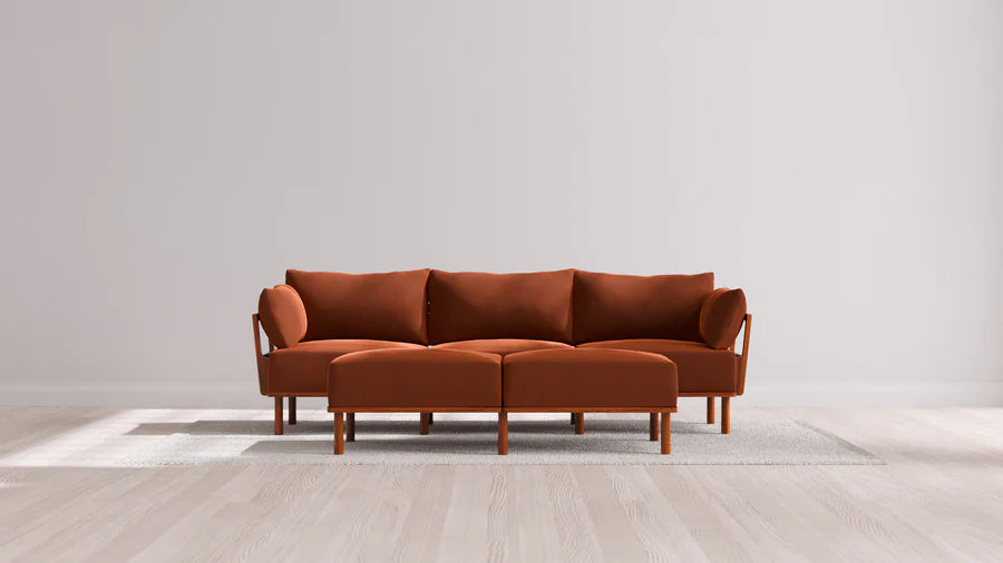 In a contemporary living room, an Indoor Jack 3-Seater Sofa with a Bench Ottoman in Balsa is elegantly placed on a light gray rug over a wooden floor, set against a plain white wall.