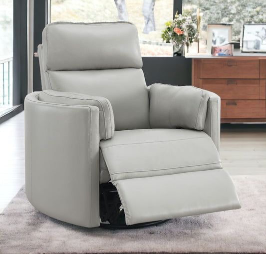 The Sagen - Chenille Glider Recliner with Swivel, in light gray, sits on a soft rug in a modern living room. Behind it are large windows and a wooden dresser adorned with framed photos and a vase of flowers, crafting a warm, cozy atmosphere.