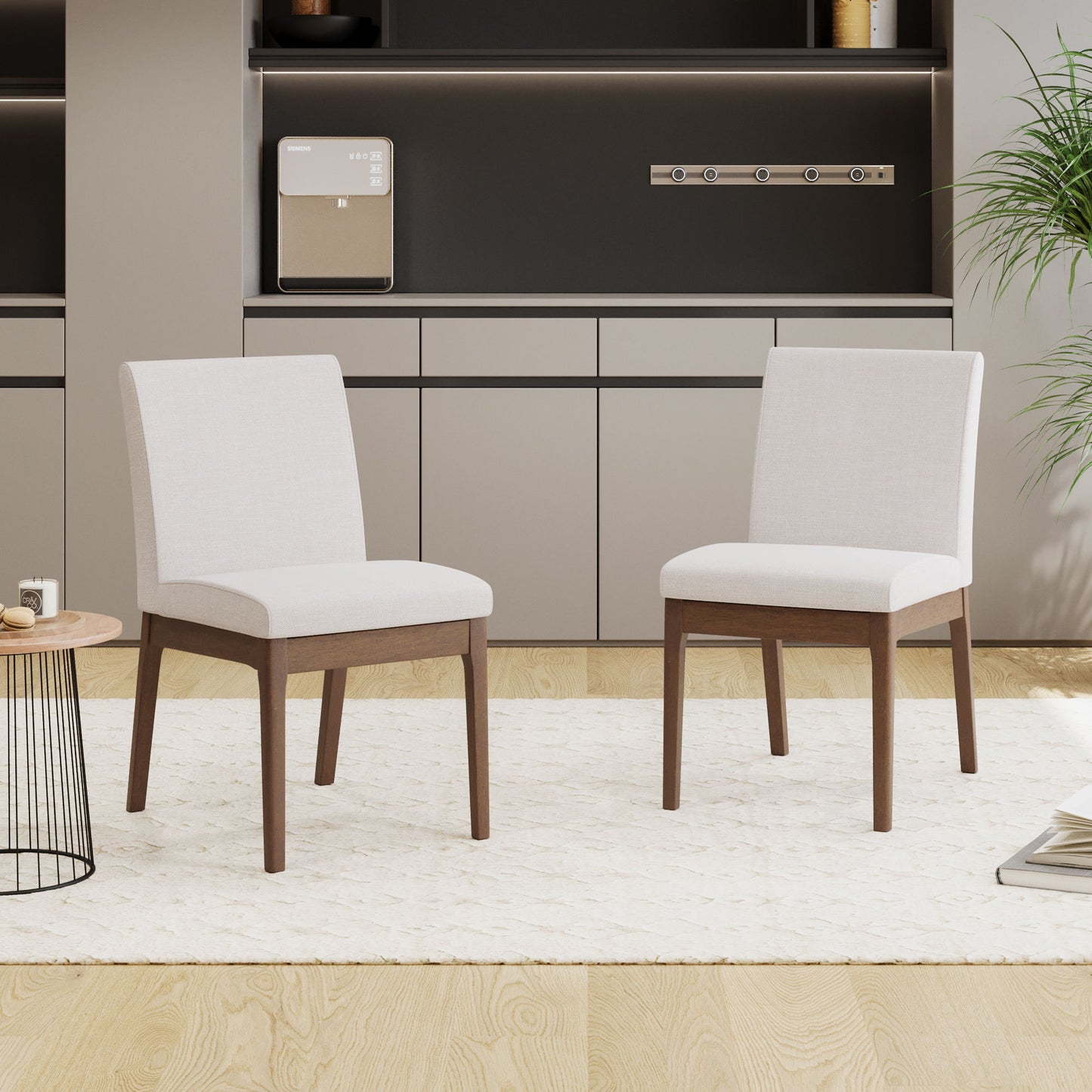 A set of two Contemporary Fabric Comfort Dining Chairs sit on a textured white rug in a minimal room with light wood floors, built-in cabinets, a small round table, and a leafy green plant.