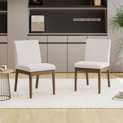 A set of two Contemporary Fabric Comfort Dining Chairs sit on a textured white rug in a minimal room with light wood floors, built-in cabinets, a small round table, and a leafy green plant.