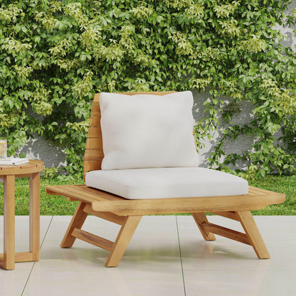 The Sedona Outdoor Club Chair with a slatted design and white cushions sits on a tiled patio next to a small wooden side table, backed by a lush green leafy wall.