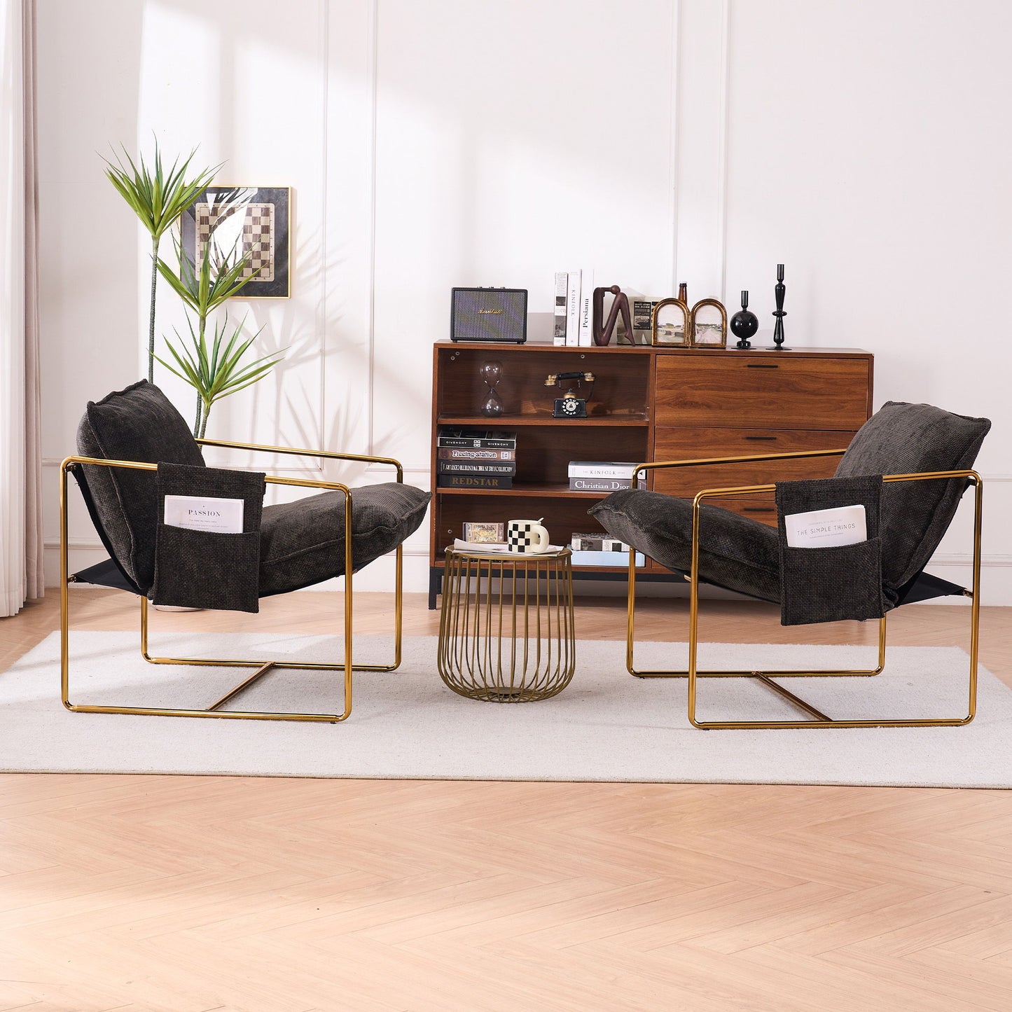 Two Upholstered Hanging Armchairs With Arm Pockets, gold-plated frames, and plush crushed foam cushions face each other across a coffee table on a light rug, with a wooden sideboard and decor in the background of a stylish living room.