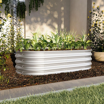 The Heavy Duty Galvanized Raised Garden Bed Kit For Vegetables, Flowers & Herbs is shown filled with leafy greens, placed on soil in a courtyard with surrounding greenery and partial sunlight.