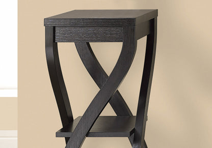 A contemporary Accent Table with a square top and X-shaped legs, featuring versatile usage and a lower shelf, is placed against a beige wall.